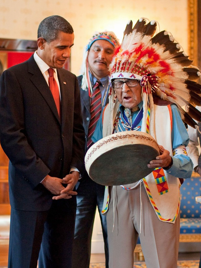 Joe Medicine Crow con il copricapo piumato mentre suona un tamburo per il presidente Obama